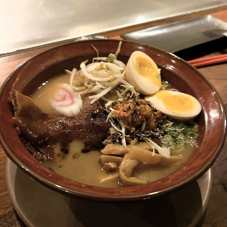 A close-up of a bowl of Shiso Noodle and Sushi Bar ramen with egg, pork, and vegetables.