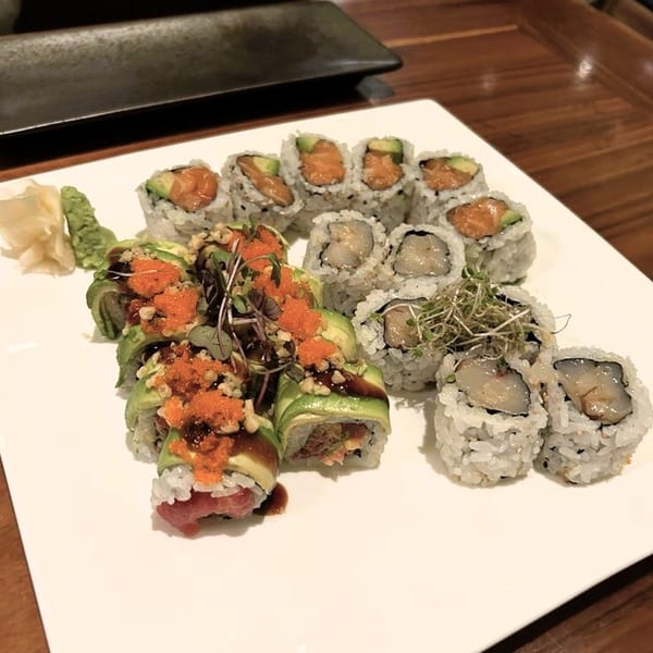 A white plate holds various sushi rolls, including salmon, tuna, and scallop, with wasabi and ginger.