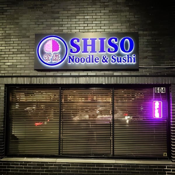 Shiso Noodle and Sushi Bar storefront at night, with a glowing blue sign and purple neon open sign.