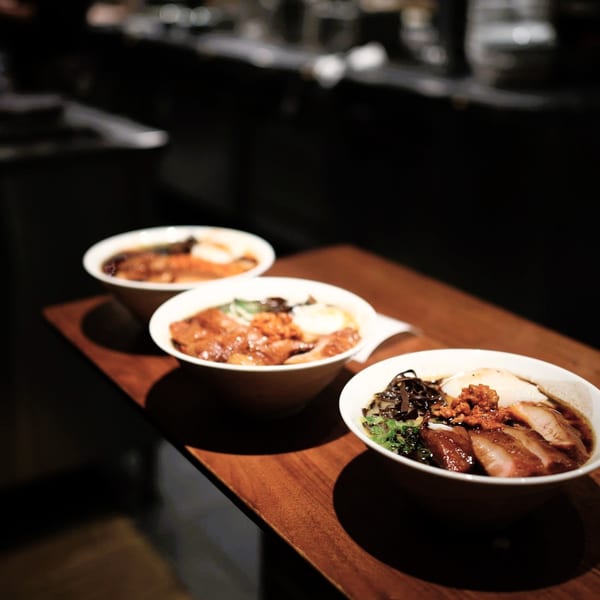 Three bowls of ramen with pork, egg, and vegetables on a dark wooden table.