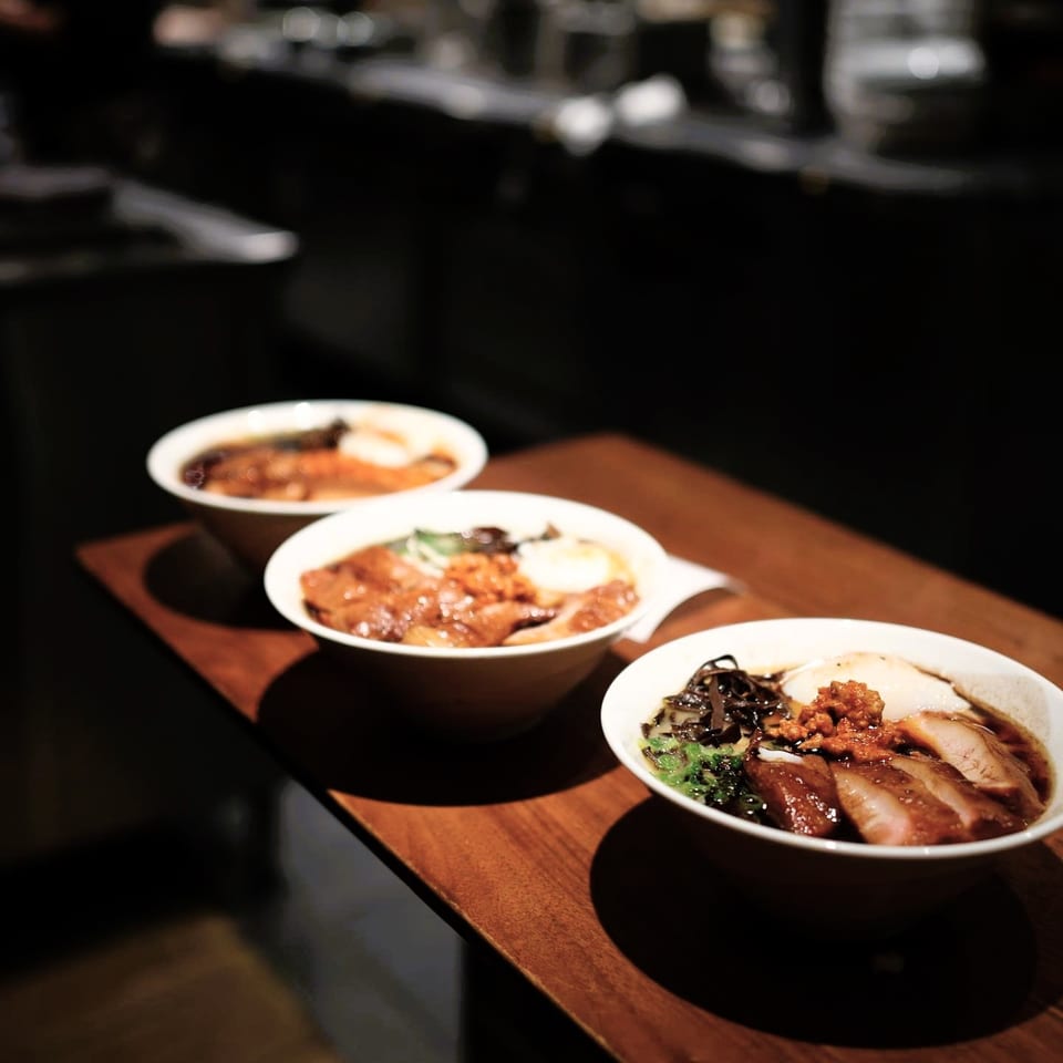 Three bowls of ramen with pork, egg, and vegetables on a dark wooden table.