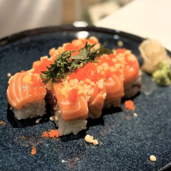 Shiso Noodle and Sushi Bar's salmon sushi rolls topped with roe, sauce, and herbs on a dark plate.